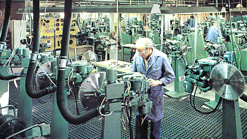 En medarbejder står i produktionen omkring mange slibemaskiner, billede taget i 70'erne.