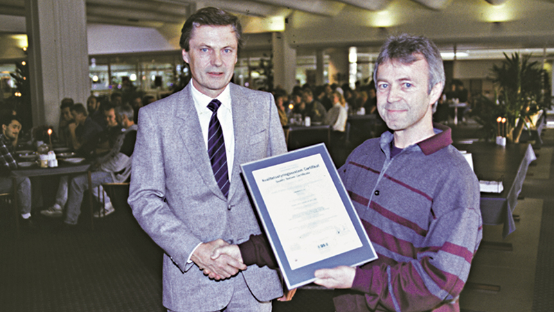 A man in a suit presents the CEO at the time with the ISO 9001 quality certification