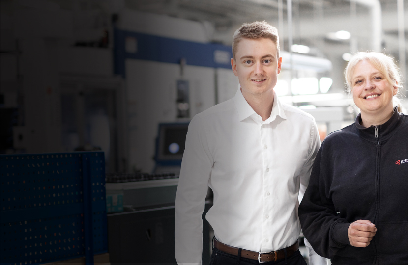 A group of three different employees are standing side by side in the production area, looking directly into the camera